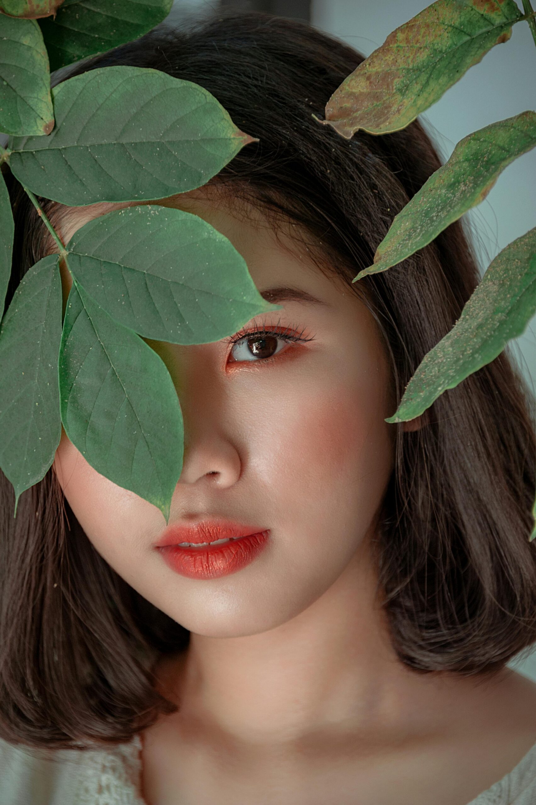 Close-up portrait of a woman peeking through green leaves, showcasing beauty and nature.